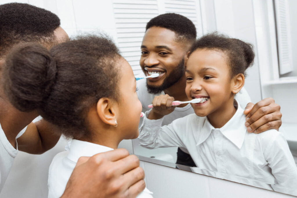 African-american girl brushing teeth with dad in bathroom